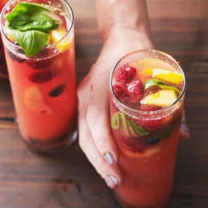 Woman grabbing one of two glasses of Fruit and Berry Sangria on a table.