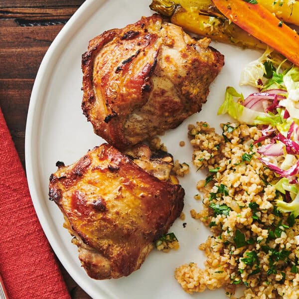 Roasted chicken thighs with Greek-style yogurt marinade on plate with side dishes.
