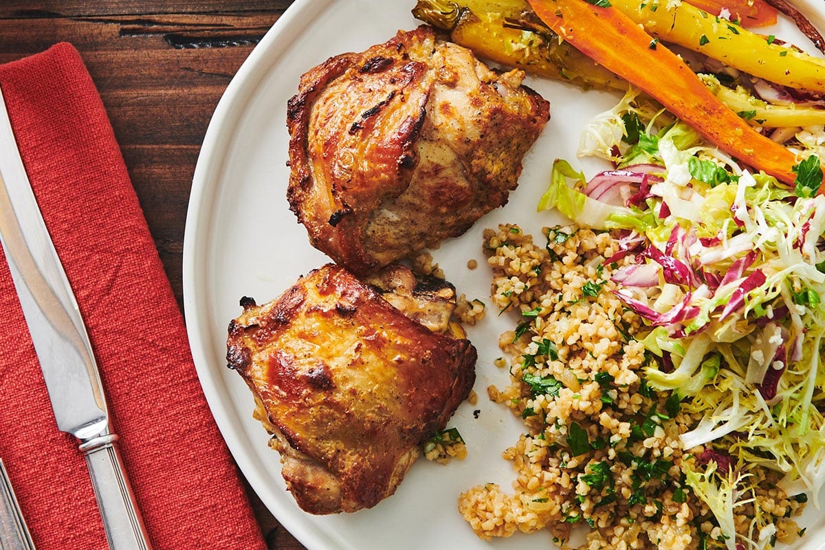 Roasted chicken thighs with Greek-style yogurt marinade on plate with side dishes.