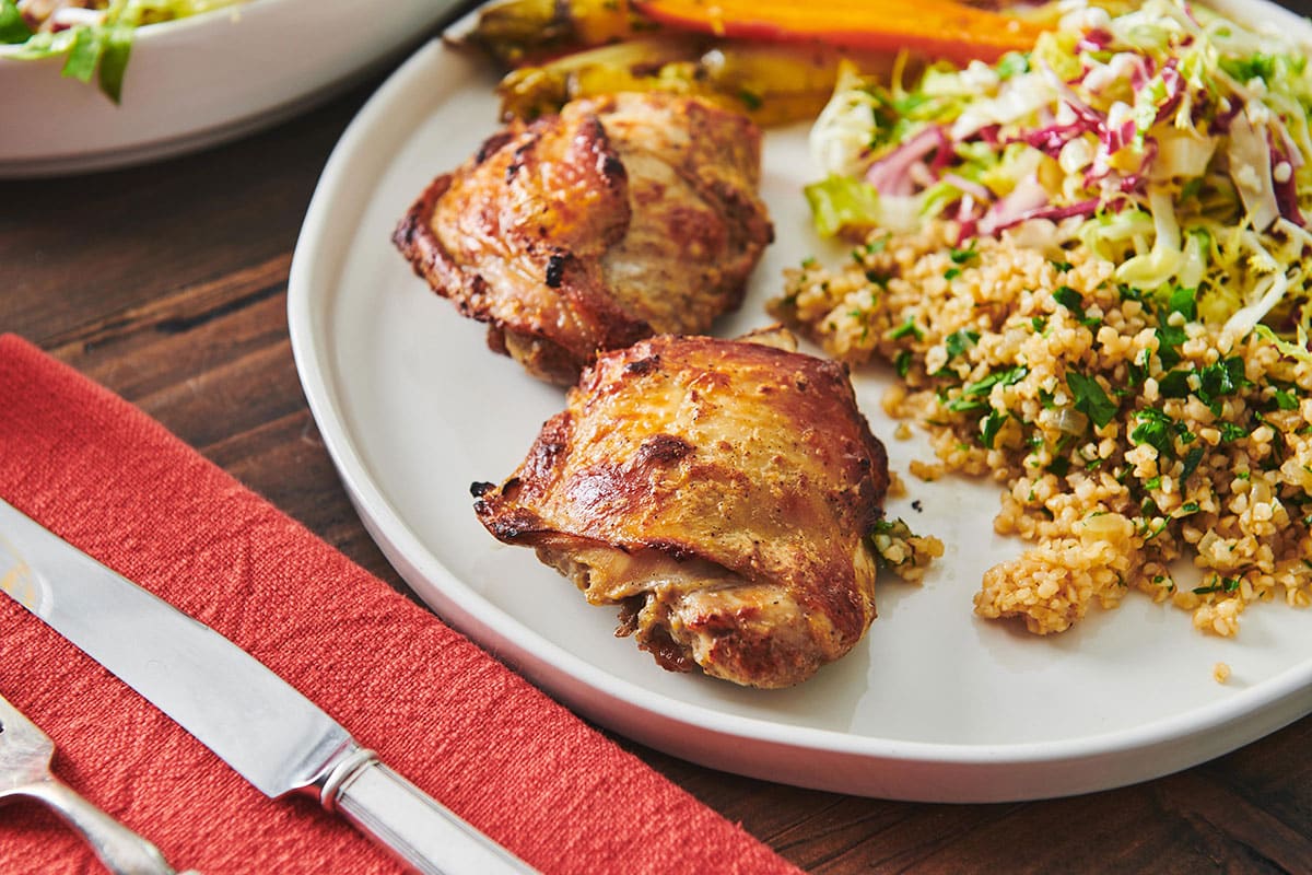 Yogurt Marinated Chicken on a plate next to a red cloth napkin with silverware.