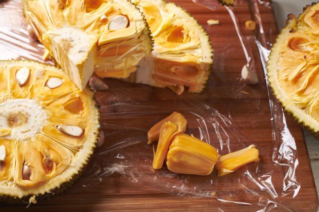 Jackfruit pods and slices of jackfruit on a wooden surface.