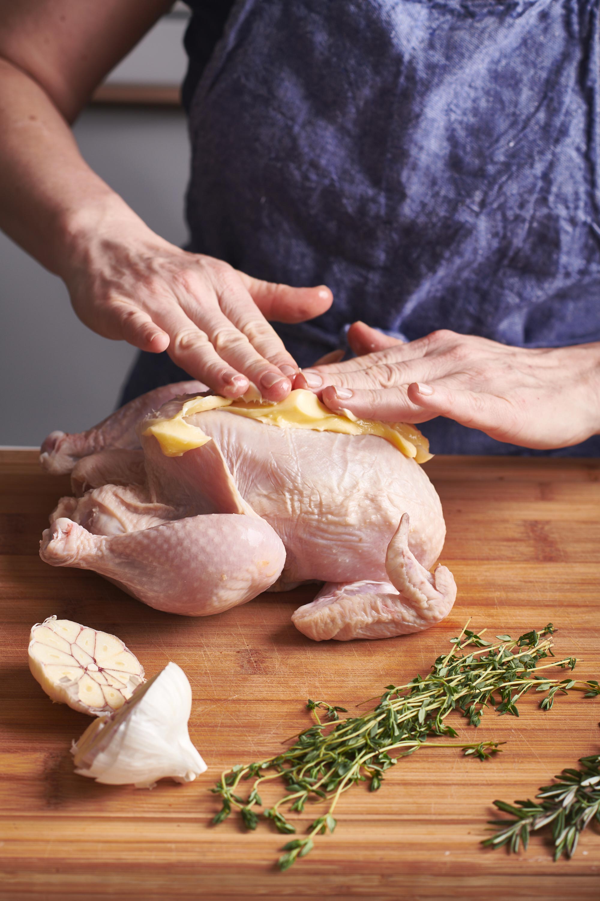Woman rubbing herbs and garlic on whole chicken.