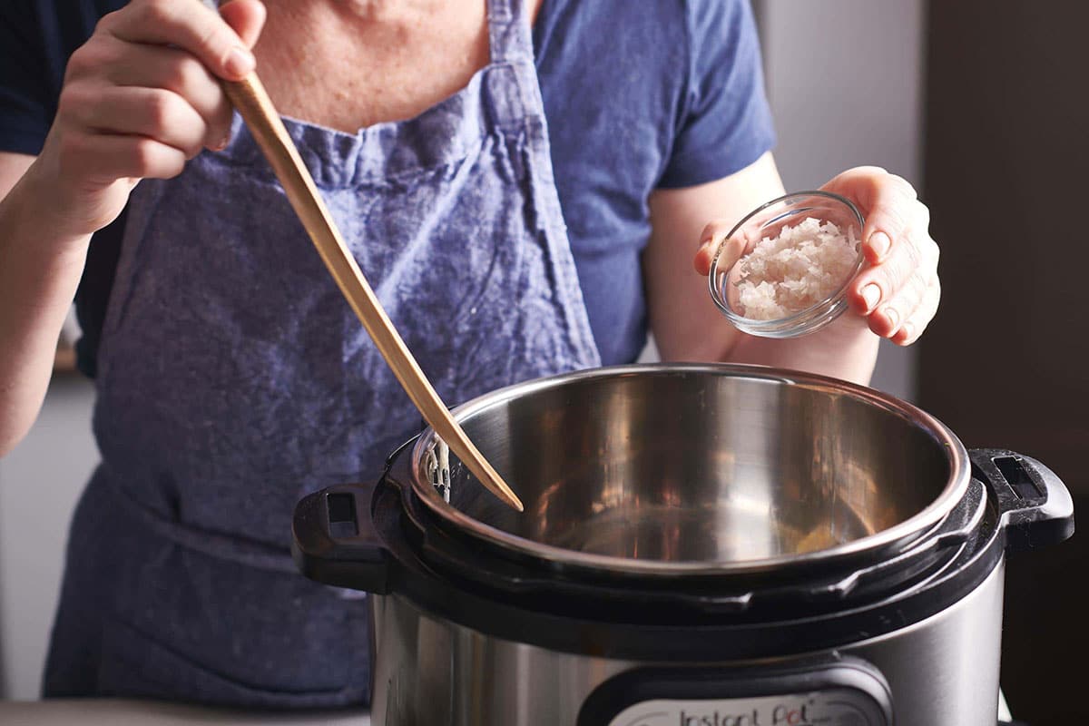 Woman adding chopped shallots to an Instant Pot.