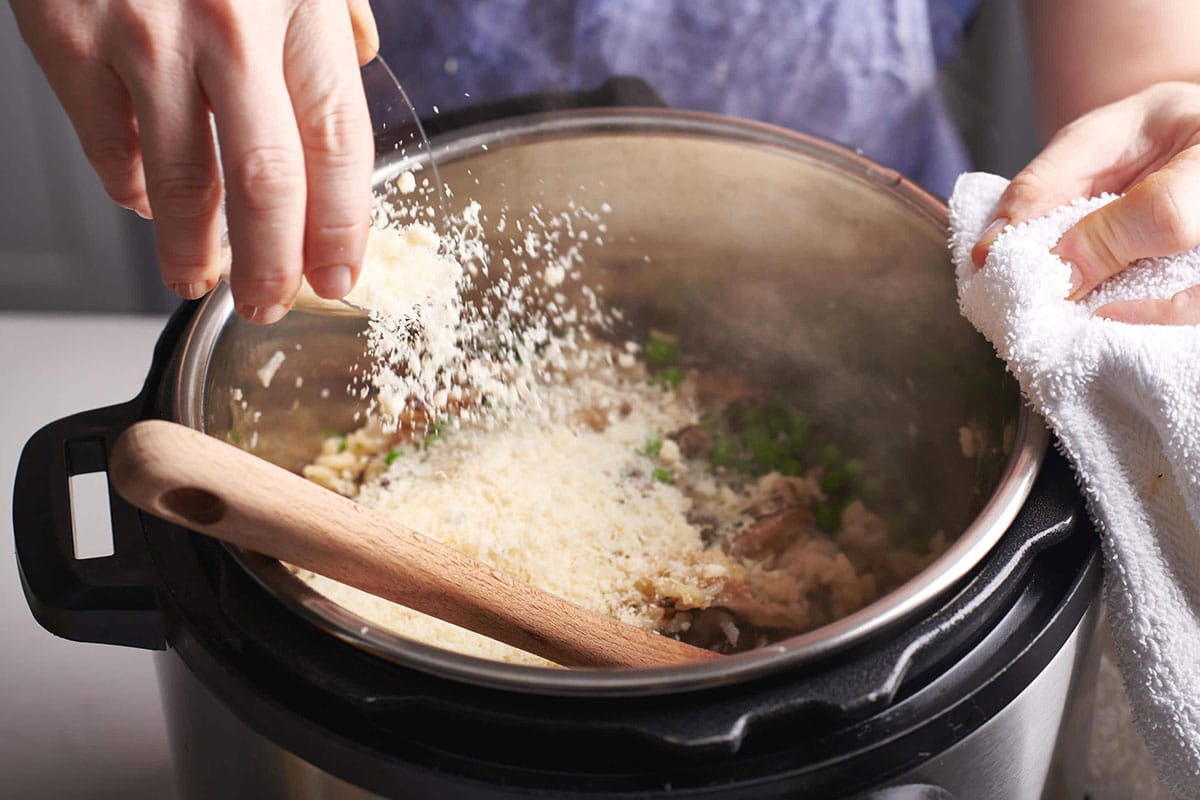 Woman tossing Parmesan cheese into an Instant Pot.