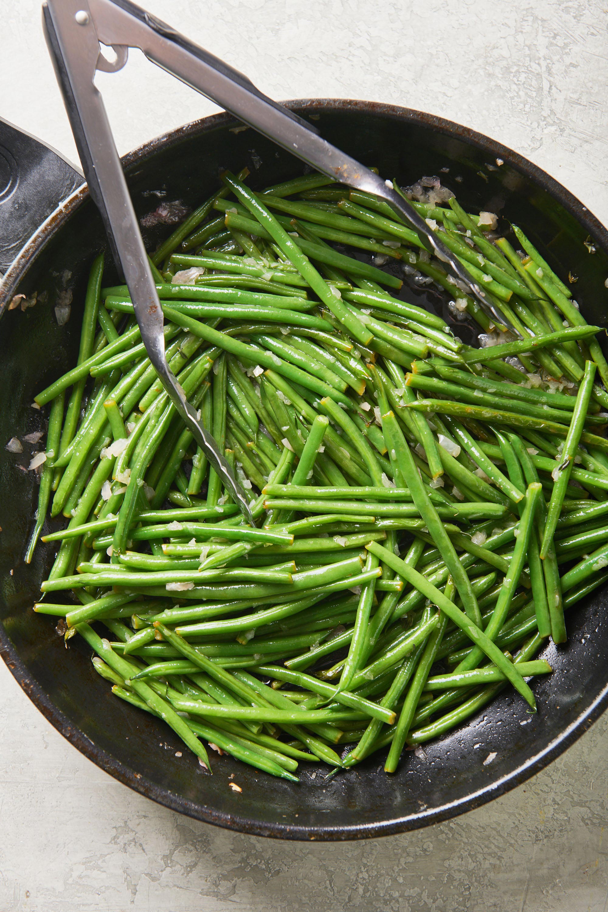 Tongs in a skillet of Sautéed Green Beans with Thyme Butter.