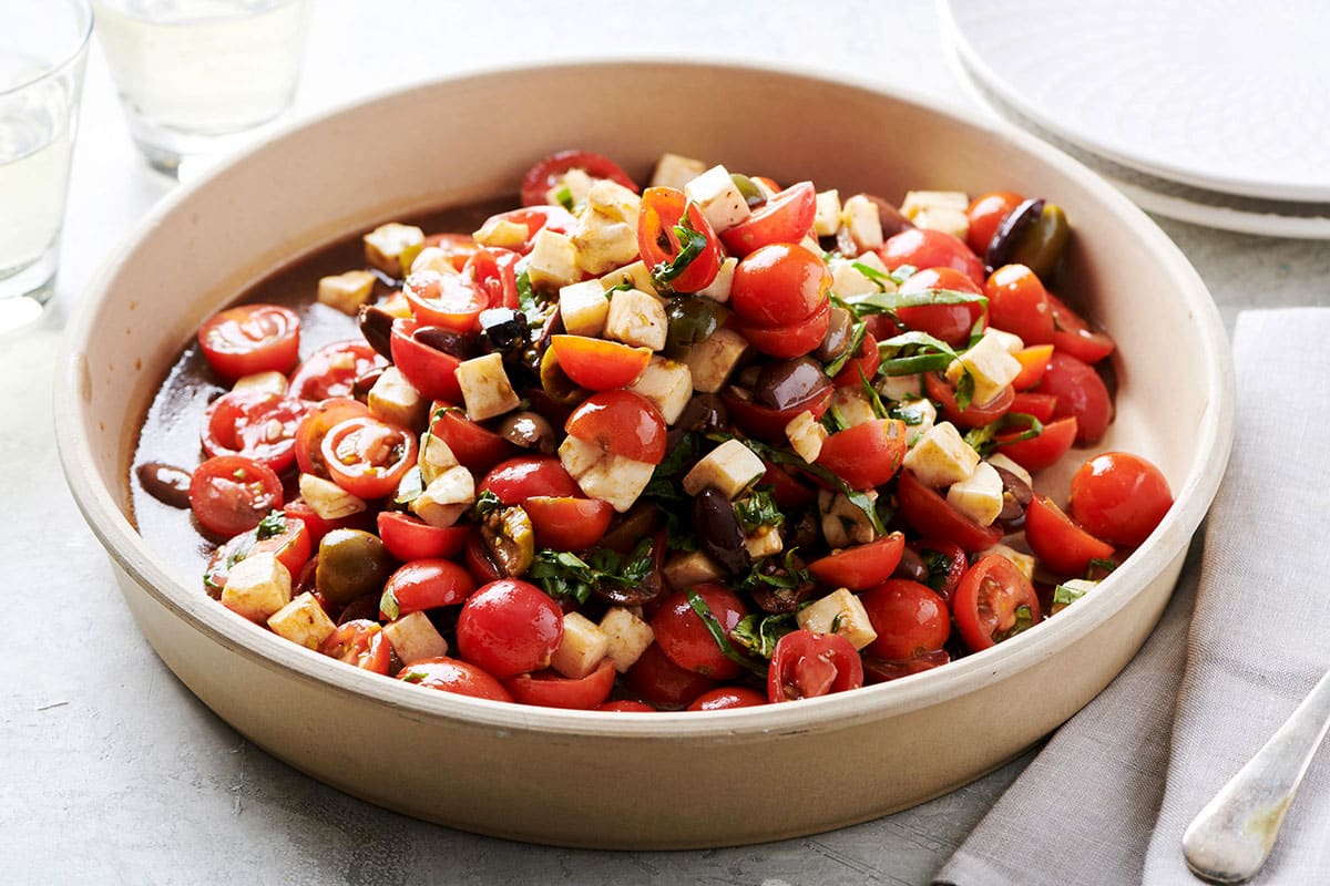 Tomato salad with mozzarella and basil in serving dish on table.