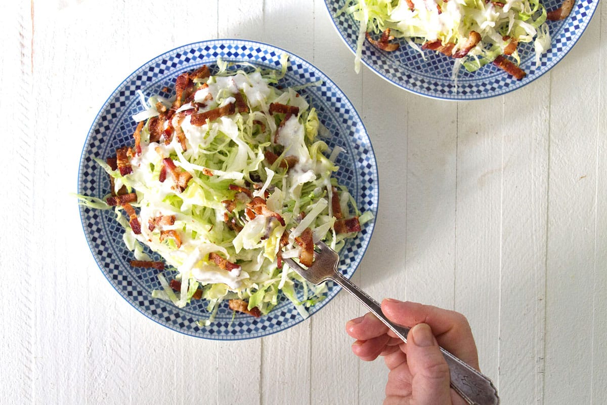 Serving wedge salad with buttermilk dressing in bowl with fork.