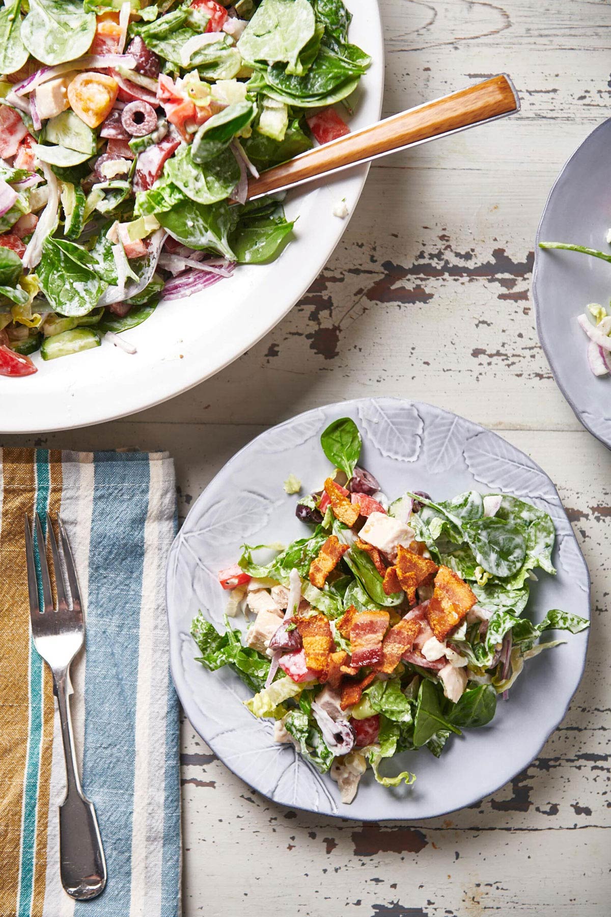 Plates of Chopped Salad with Chicken and Blue Cheese Dressing on a white, wooden table.