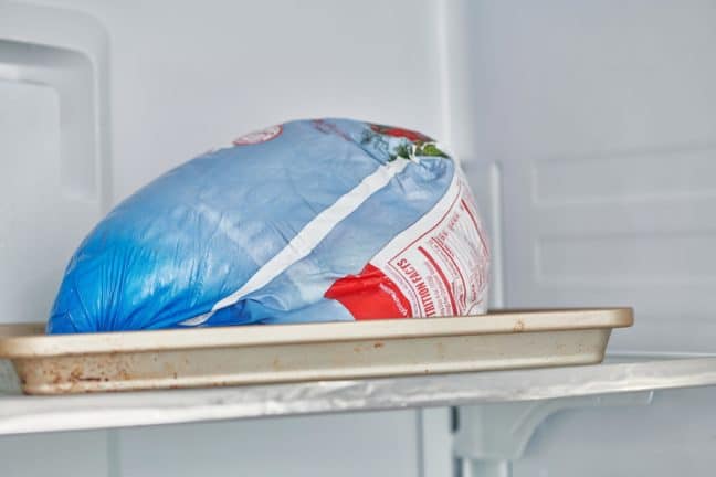 Wrapped turkey on a tray in a refrigerator.