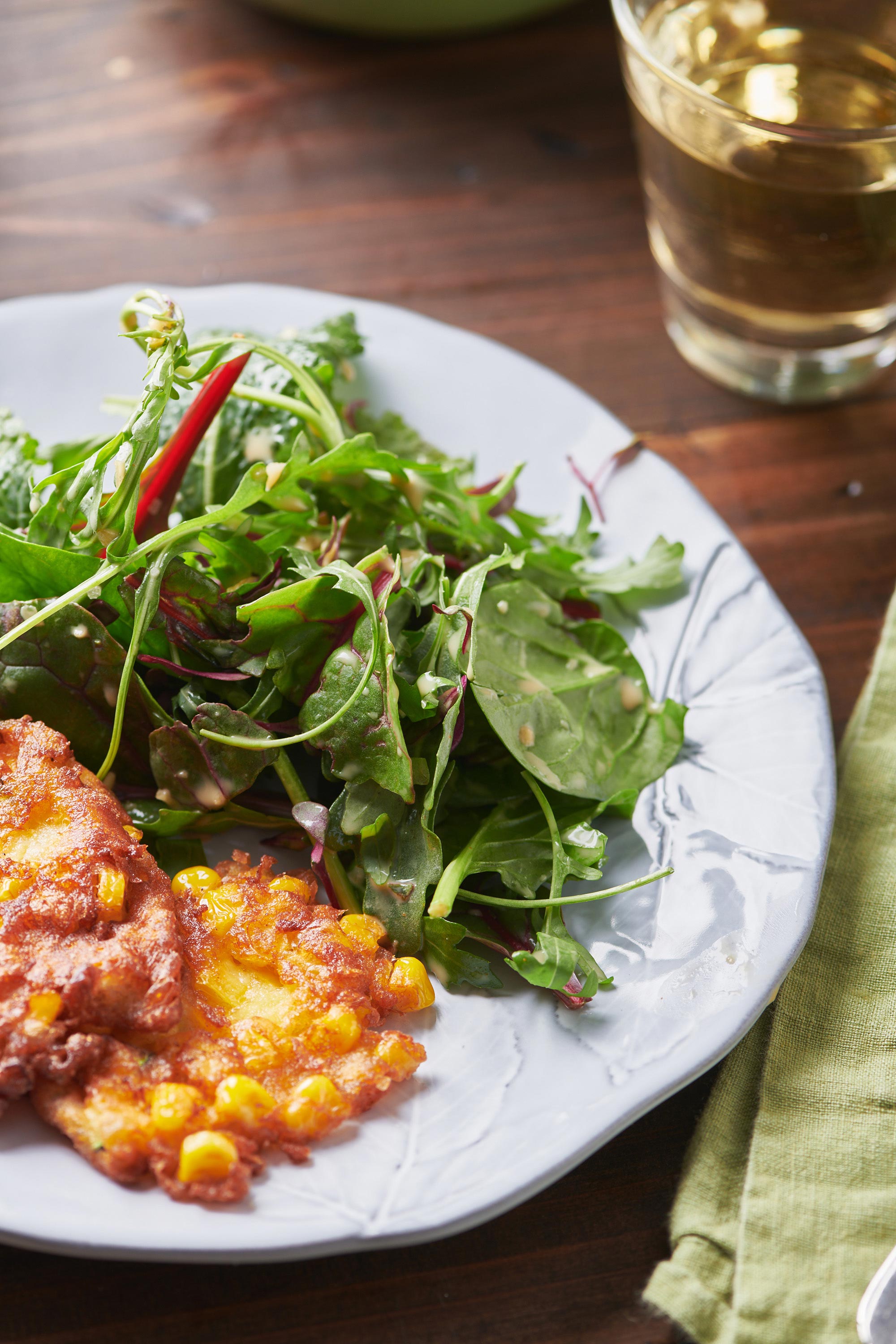 Mixed Green Salad with Creamy Sesame Dressing on plate with corn fritters.