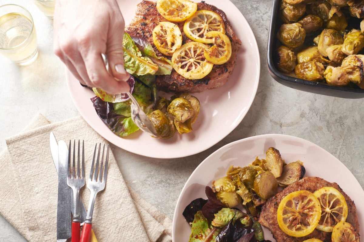 Woman placing brussels sprouts on a plate with salad and a Spanish Pork Chop.