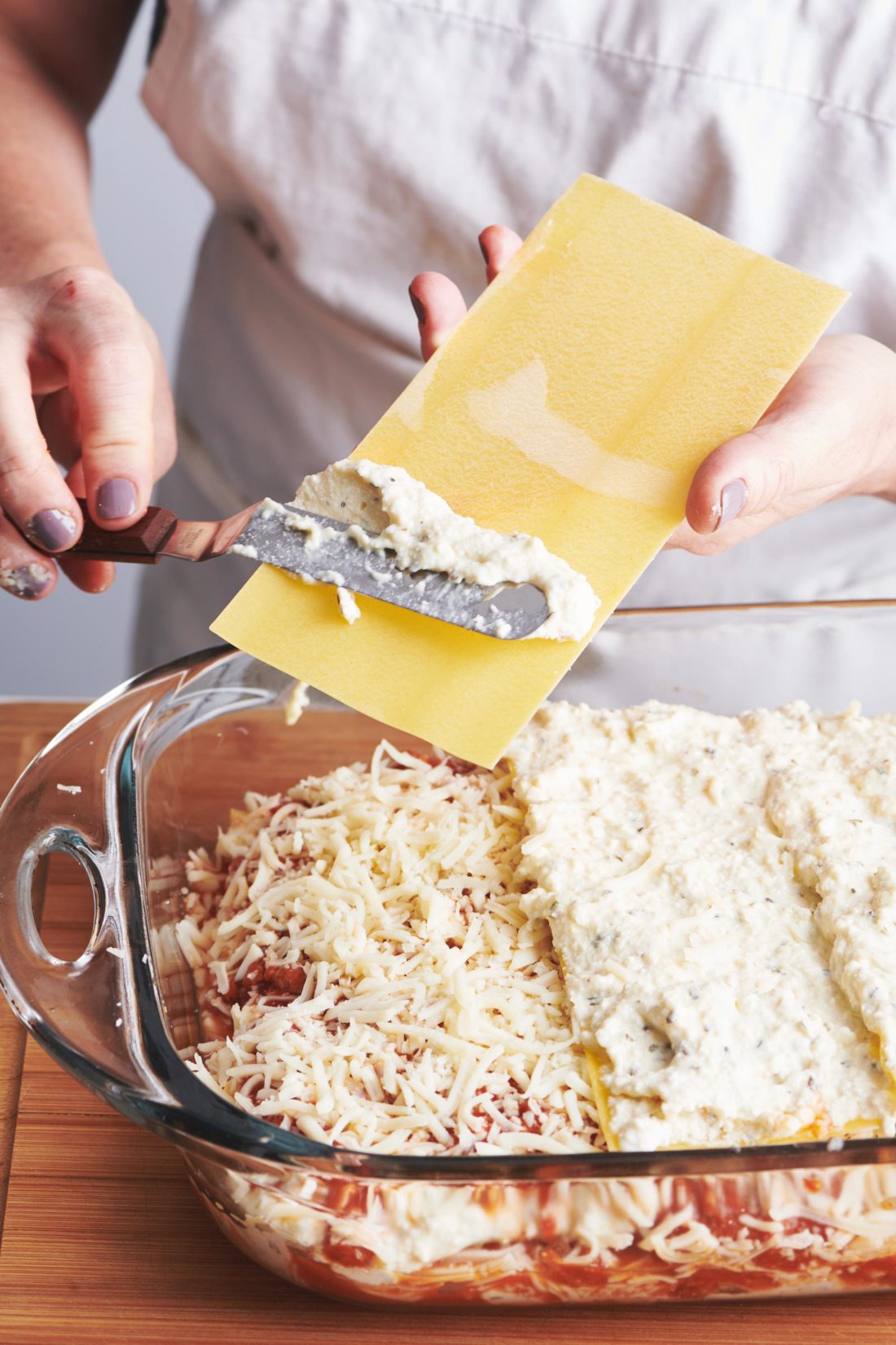 Knife spreading ricotta mixture on a lasagna noodle.