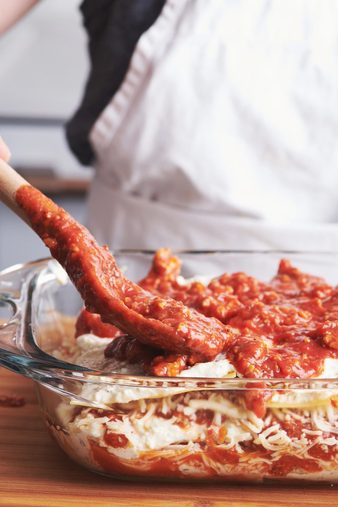 Spoon spreading tomato sauce onto a baking pan of turkey lasagna.