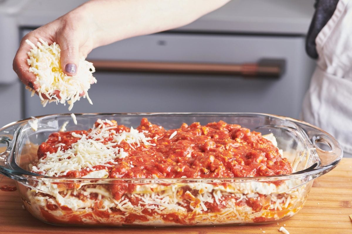 Woman sprinkling mozzarella cheese onto a baking dish of turkey lasagna.