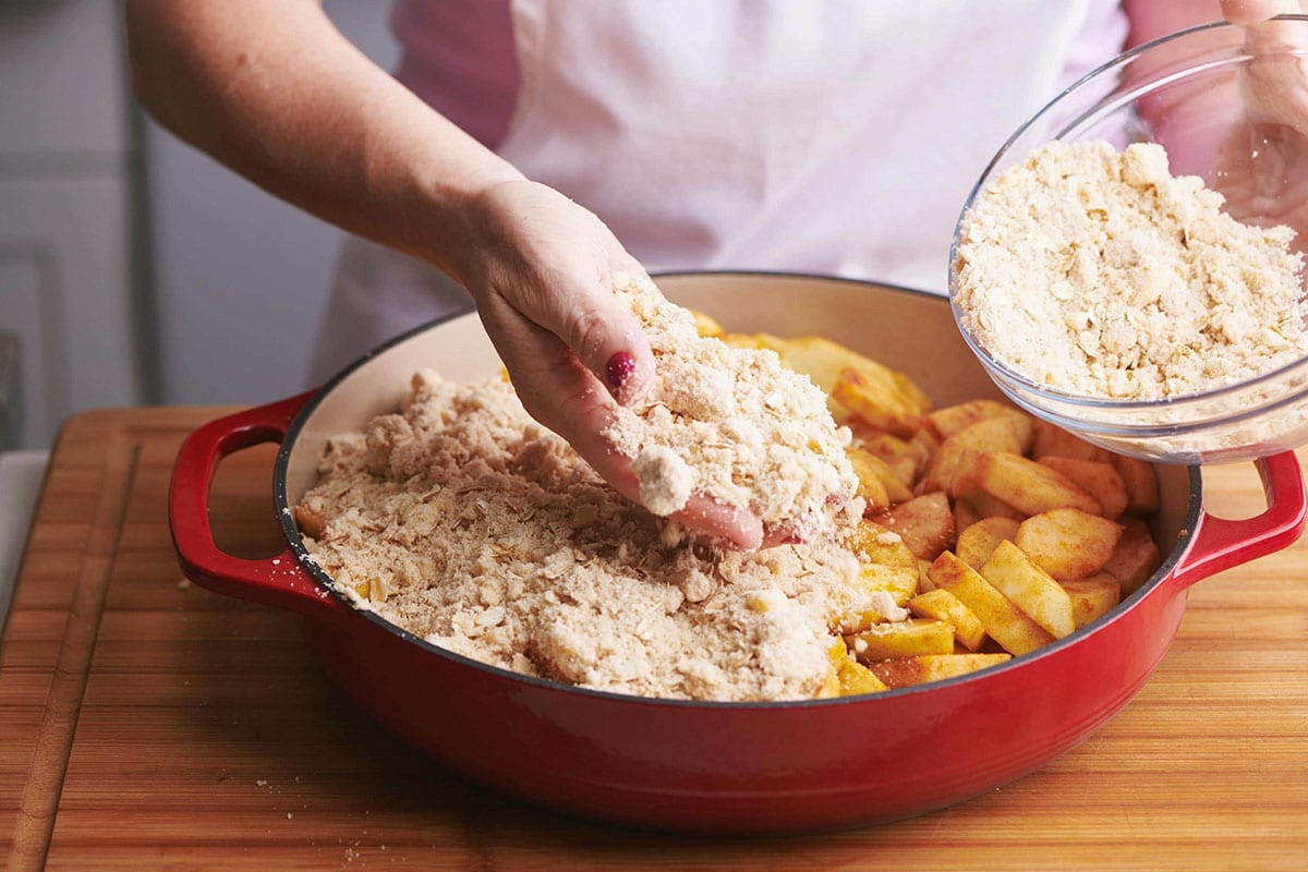 Adding homemade streusel topping to sliced apples in baking dish.