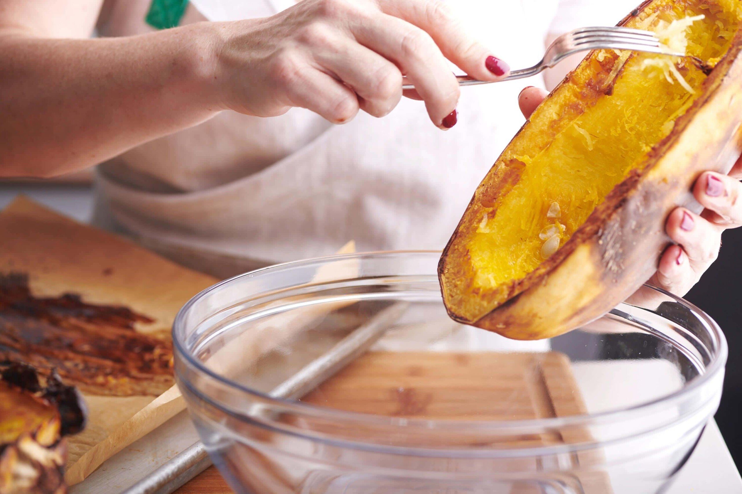 Woman scraping the inside of a spaghetti squash with a fork.