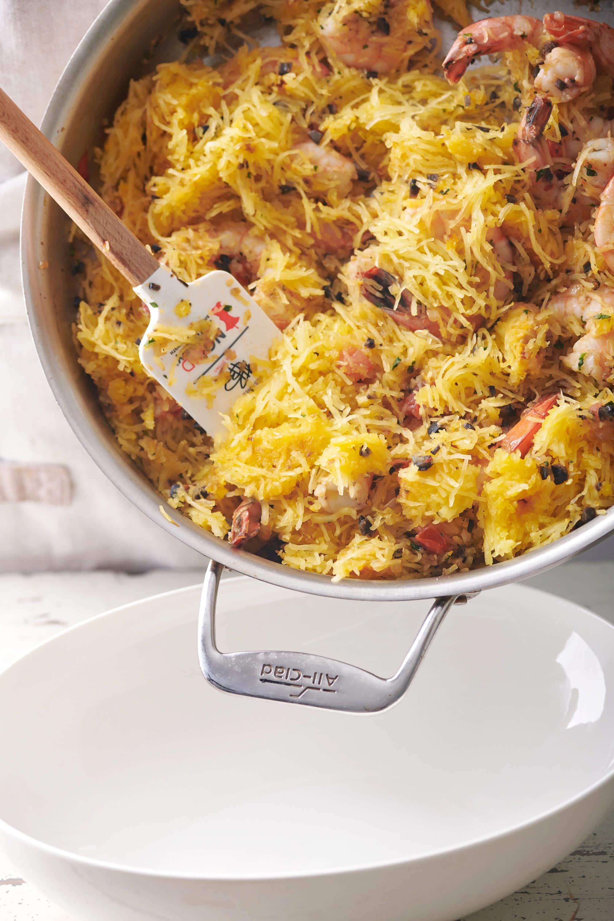 Spatula taking Greek-Style Spaghetti Squash with Shrimp from a skillet into a bowl.