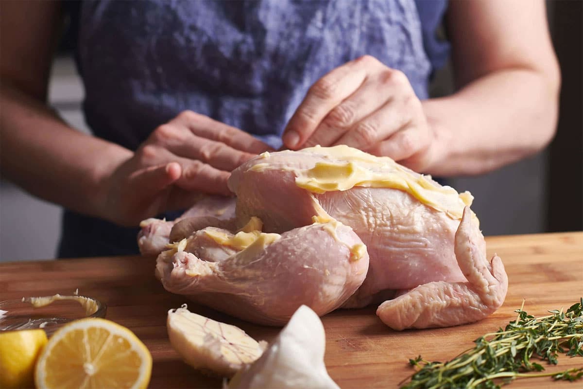 Woman spreading butter on whole raw chicken.