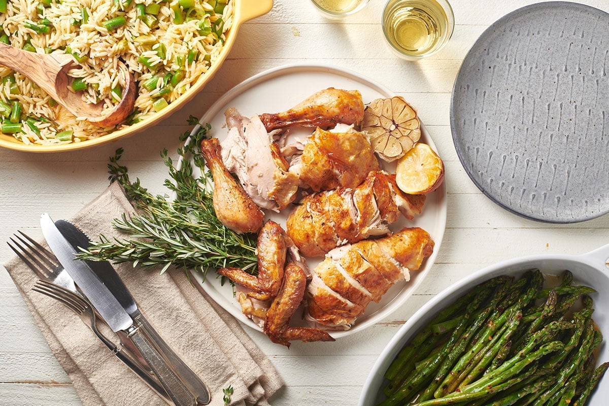Roasted chicken on plate and platter with asparagus and rice.