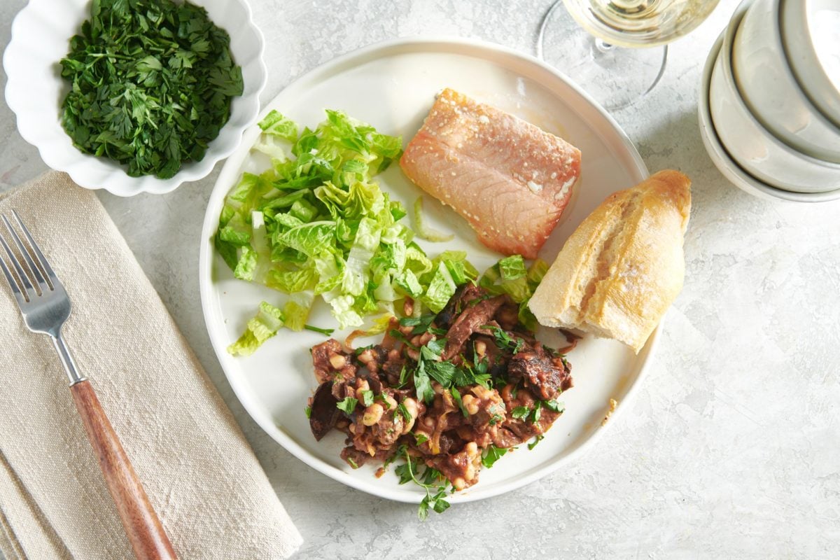 Fish, salad, bread, and Mushroom, Tomato and White Bean Ragout on a white plate.