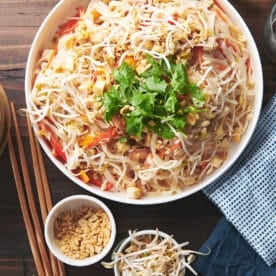 Large, white serving bowl of Pad Thai on a wooden table.