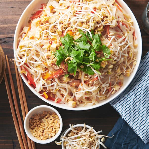 Large, white serving bowl of Pad Thai on a wooden table.