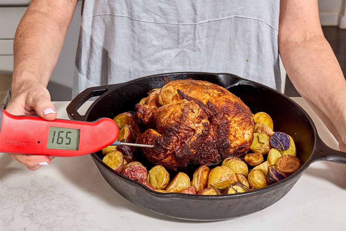 Woman testing roast chicken with red Thermapen thermometer.