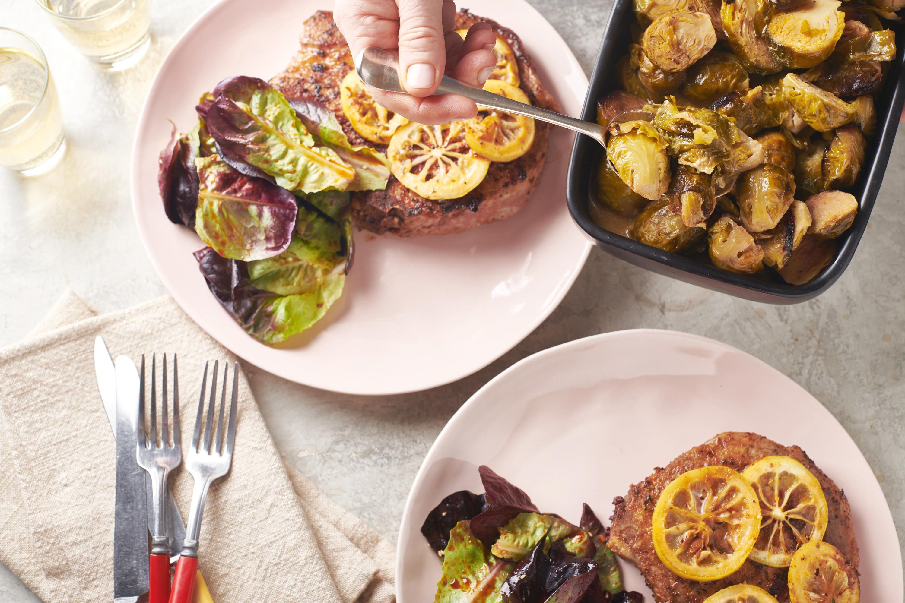 4-Ingredient Slow Cooker Maple-Dijon Brussels Sprouts being spooned onto a plate with pork chop.