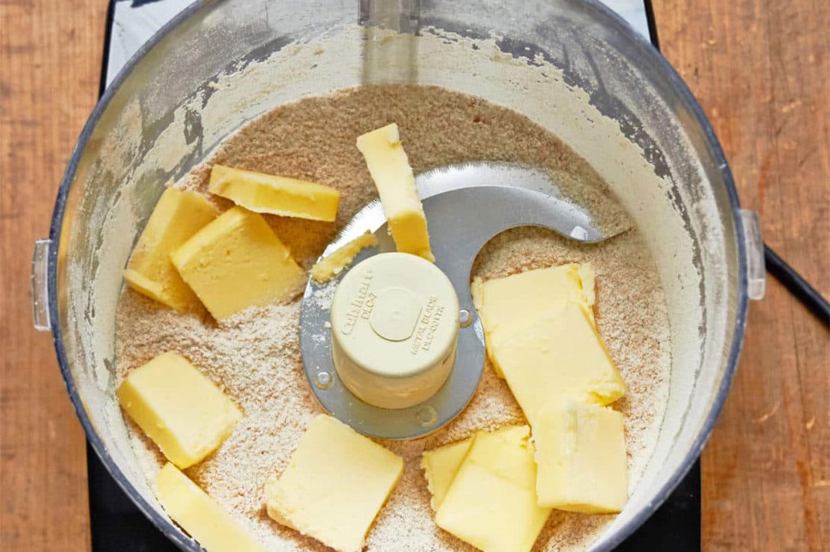Slices of butter over flour mixture in food processor.