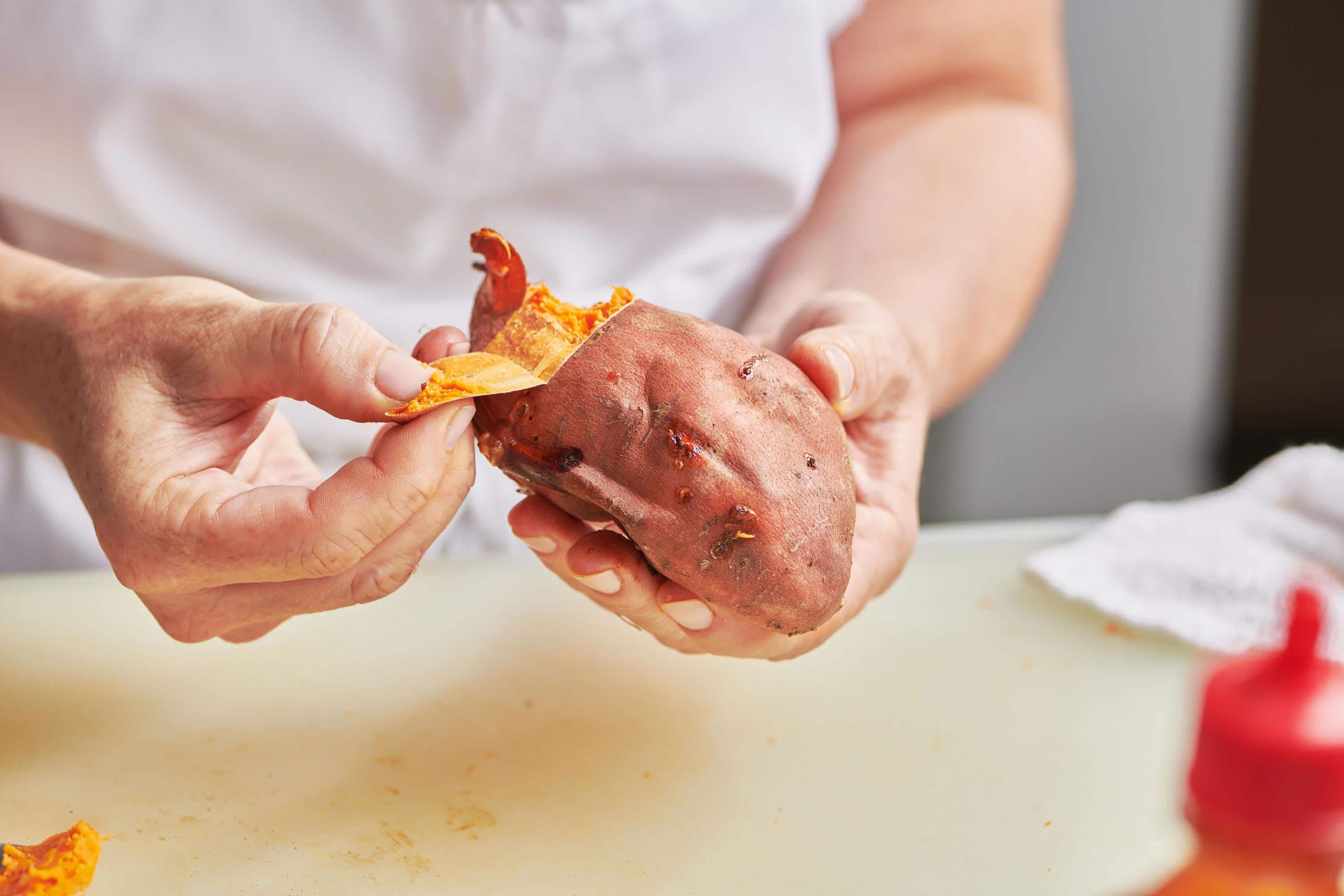 Woman using her hands to pull the peel off of a cooked sweet potato.