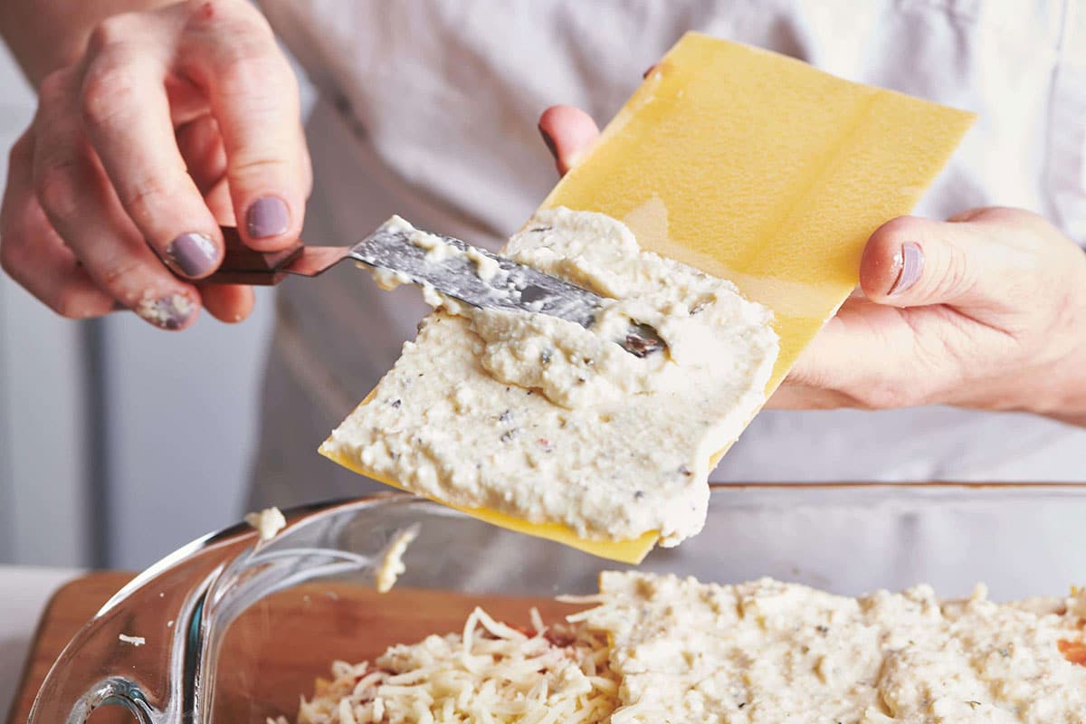 Woman spreading herb-seasoned ricotta on no-bake lasagna noodles.