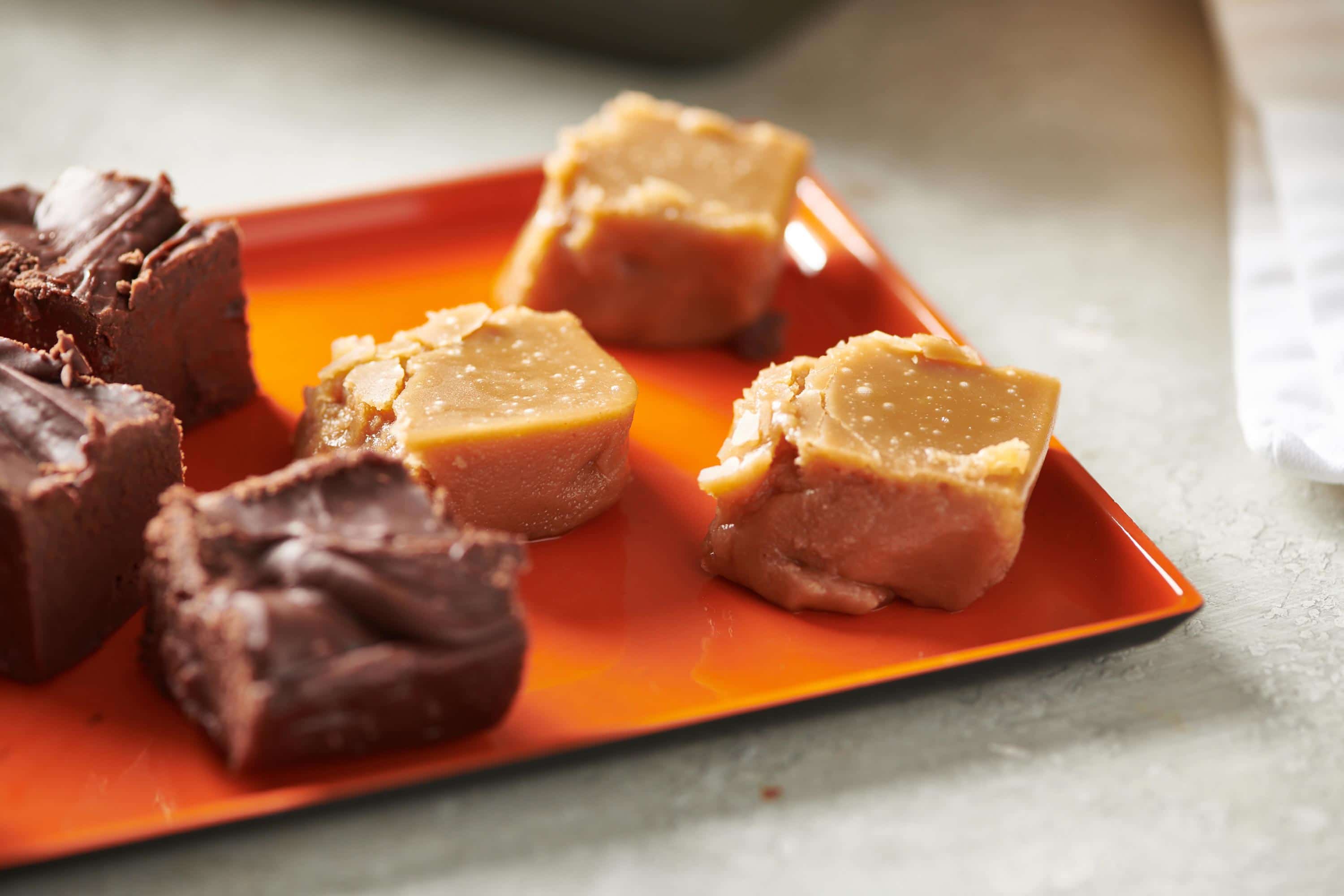 Squares of Brown Sugar Fudge and other fudge on an orange plate.