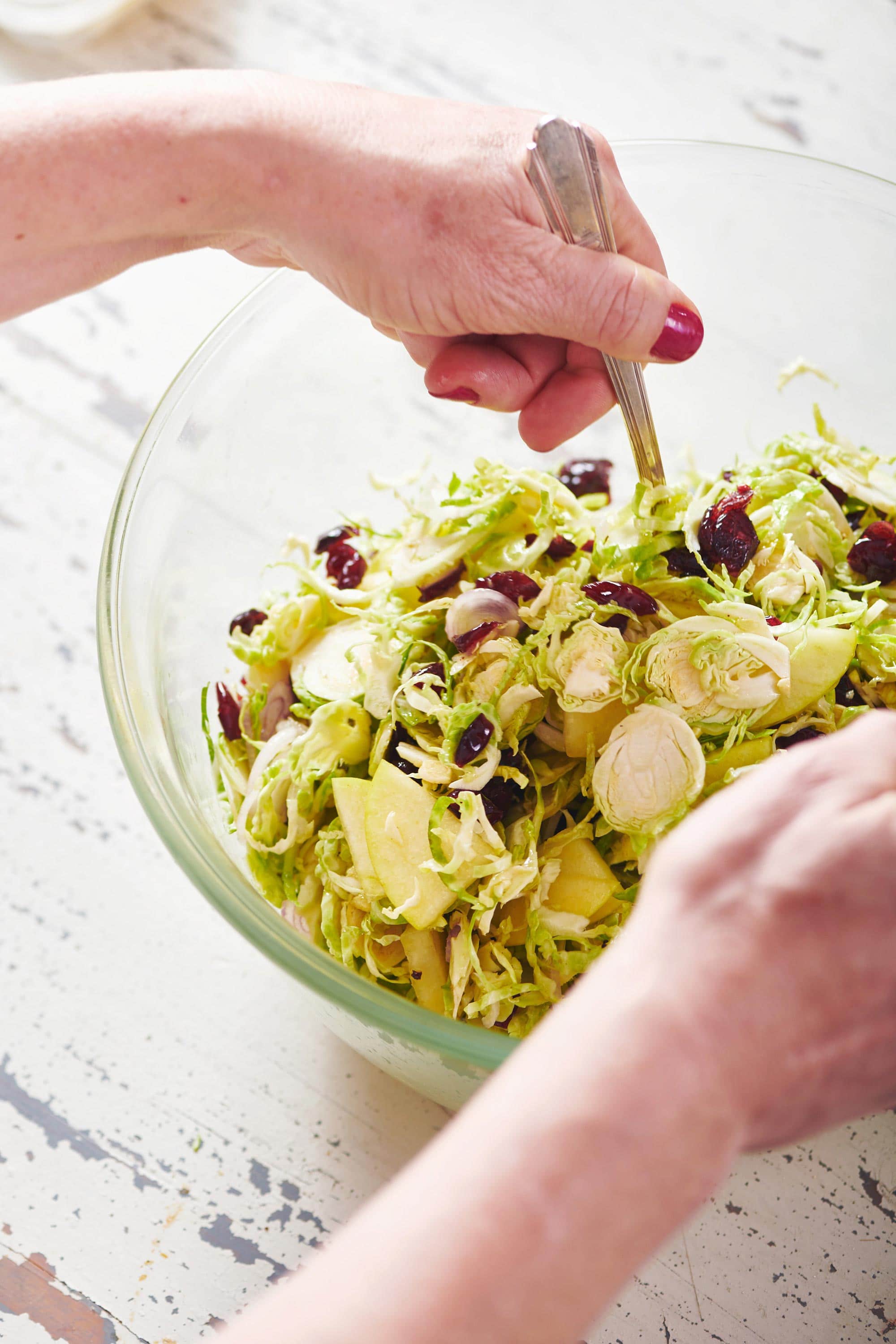 Woman tossing a Brussels Sprouts, Pecorino and Apple Salad with dressing.