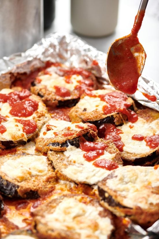 Spoon topping eggplant slices with tomato sauce.
