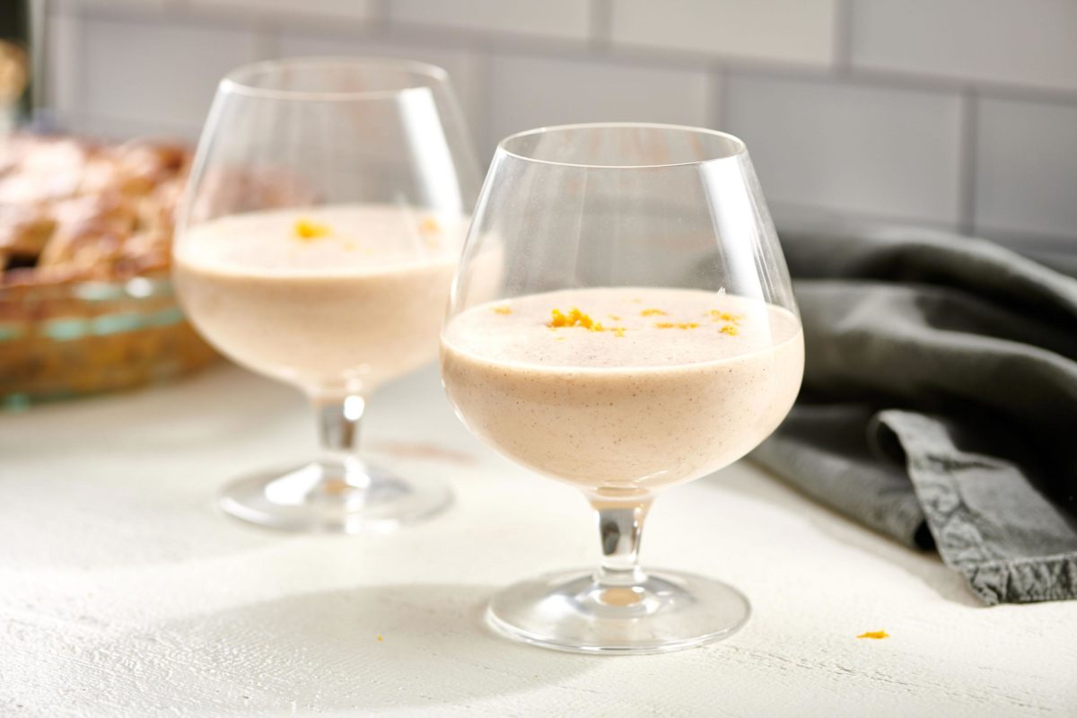 Two stemmed glasses of eggless Egg Nog on a countertop.