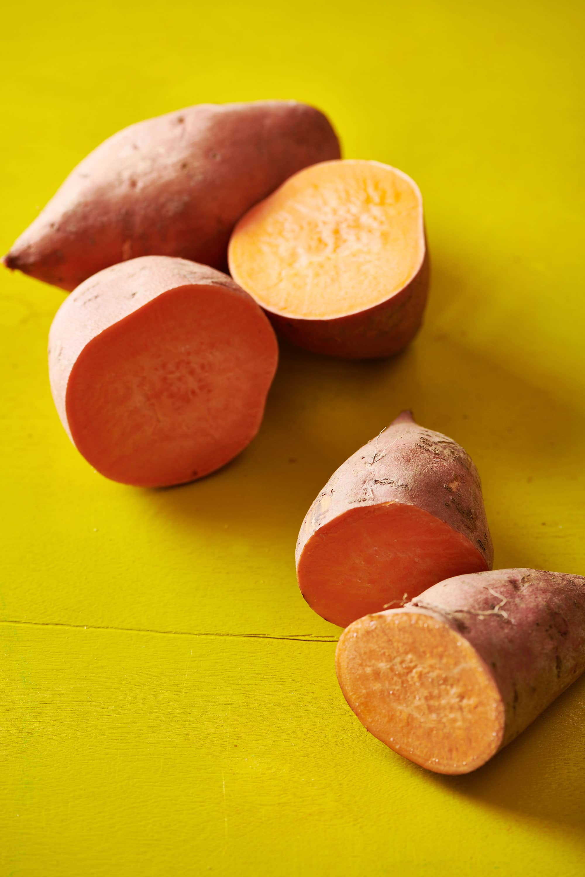 Halved sweet potatoes on a yellow table.