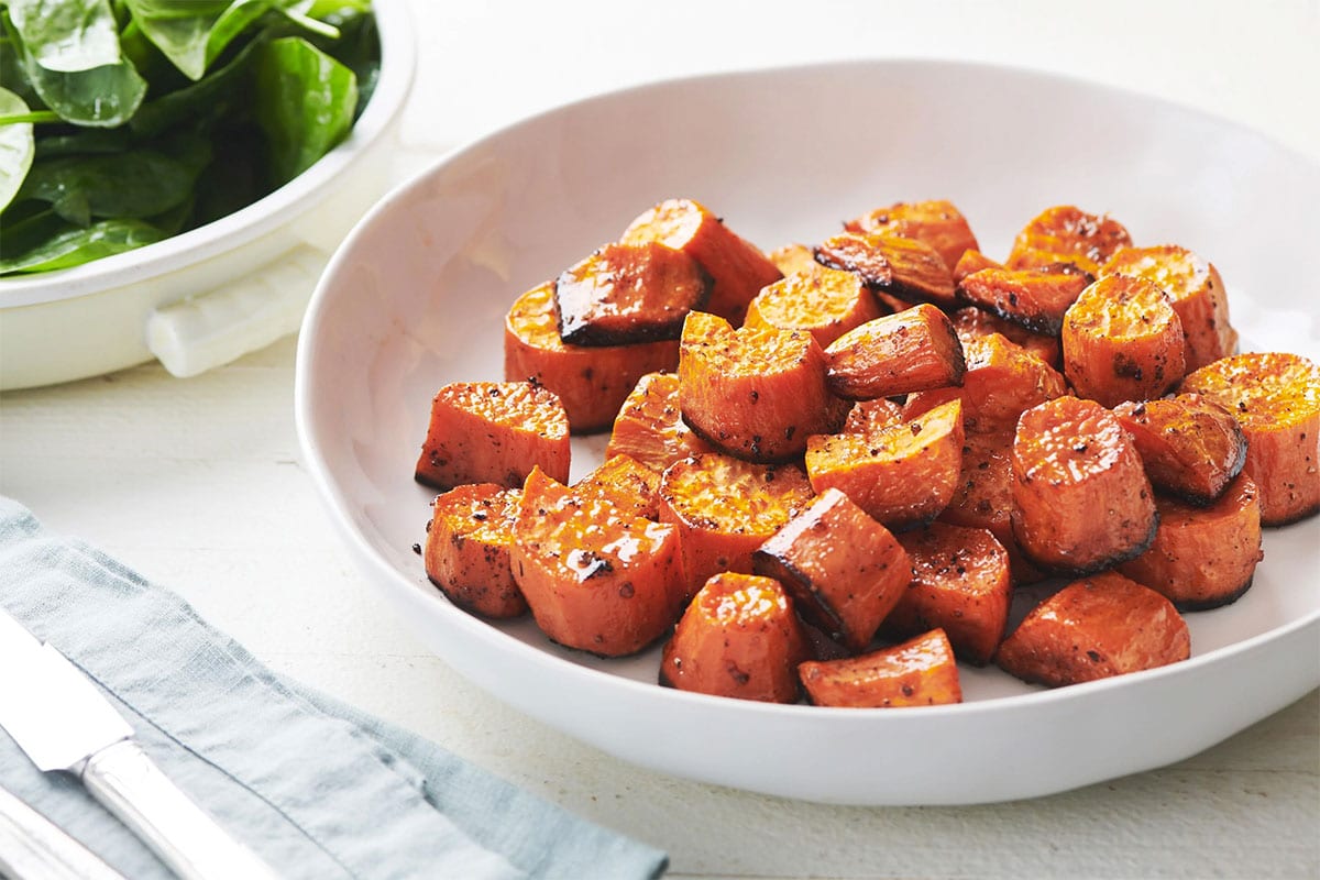 Butter roasted sweet potatoes in white serving dish on table.