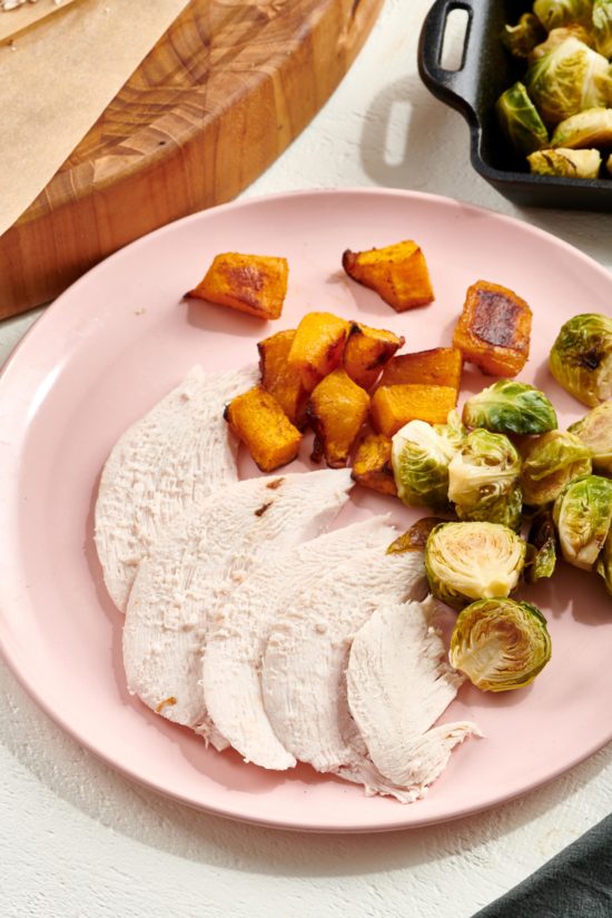 Turkey Breast, brussels sprouts, and sweet potatoes on a pink plate.