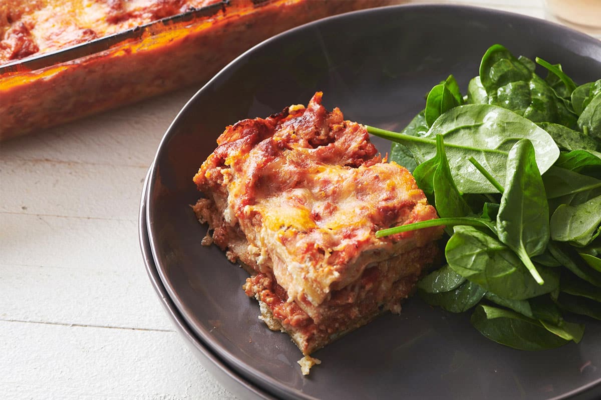 Slice of turkey lasagna on brown plate with salad.