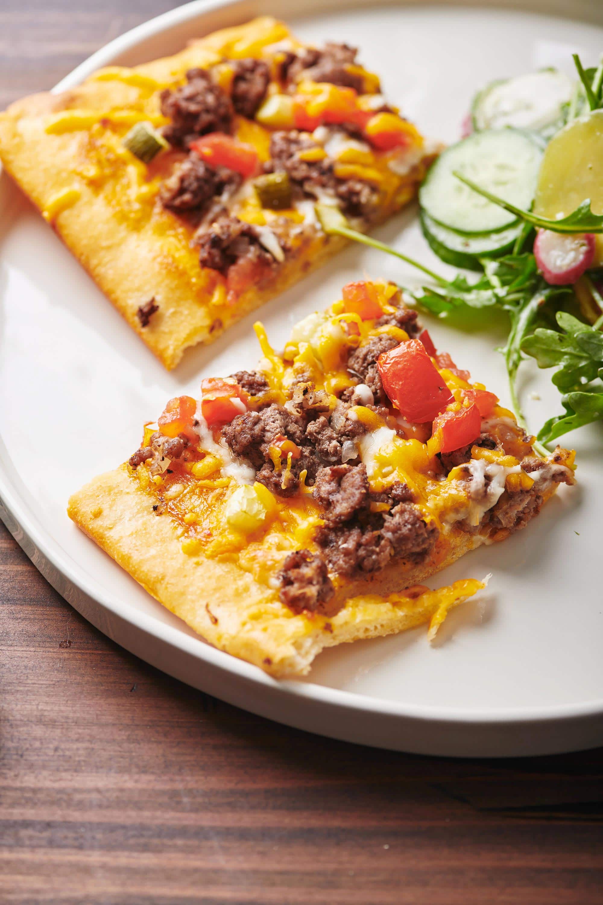 Salad on a plate with slices of Cheeseburger Pizza.