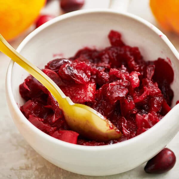 Cranberry orange relish in white bowl with yellow spoon.