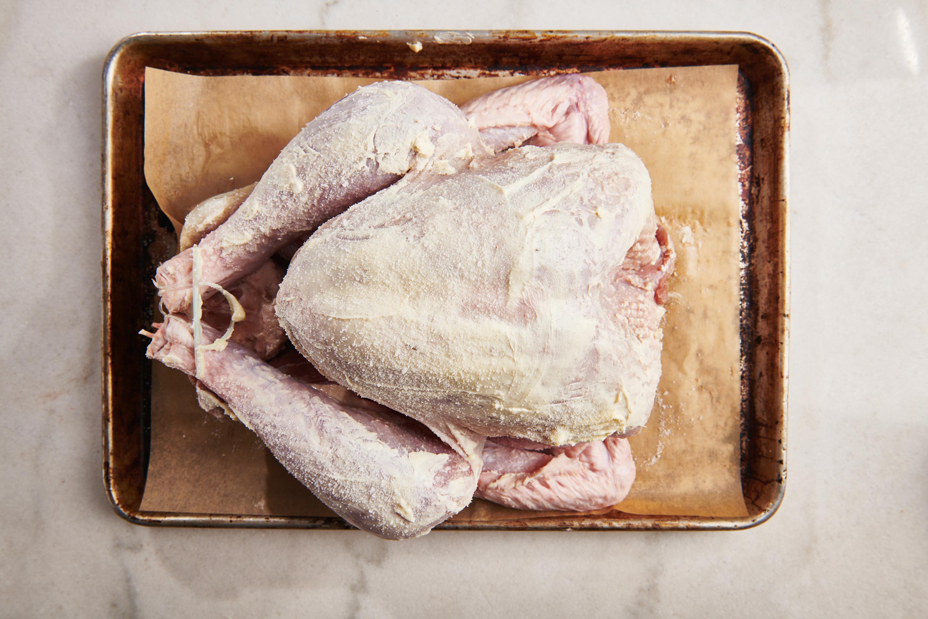 Uncooked trussed turkey smeared with butter on a baking sheet.