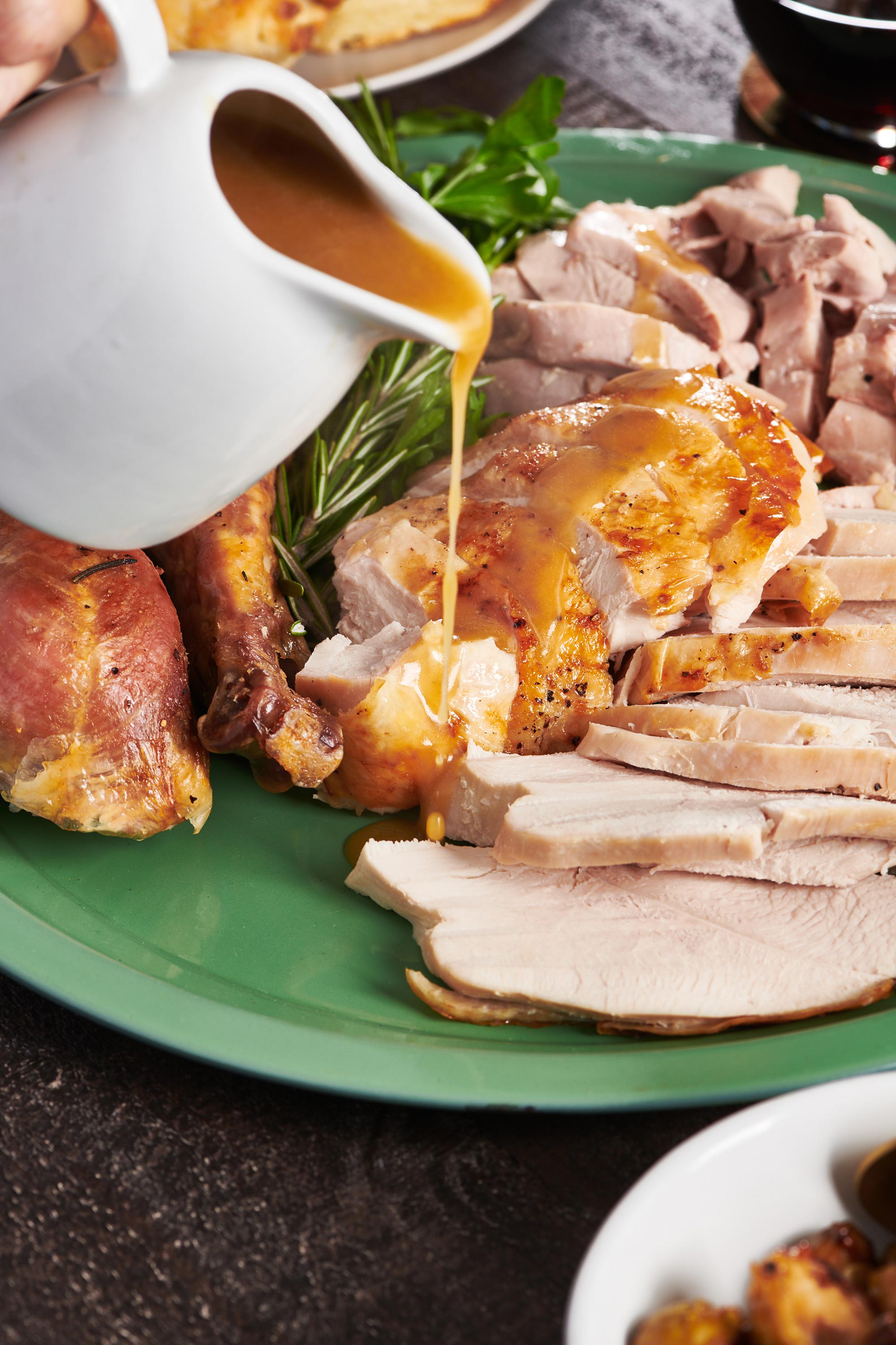 Gravy being poured over sliced turkey on a green plate. 