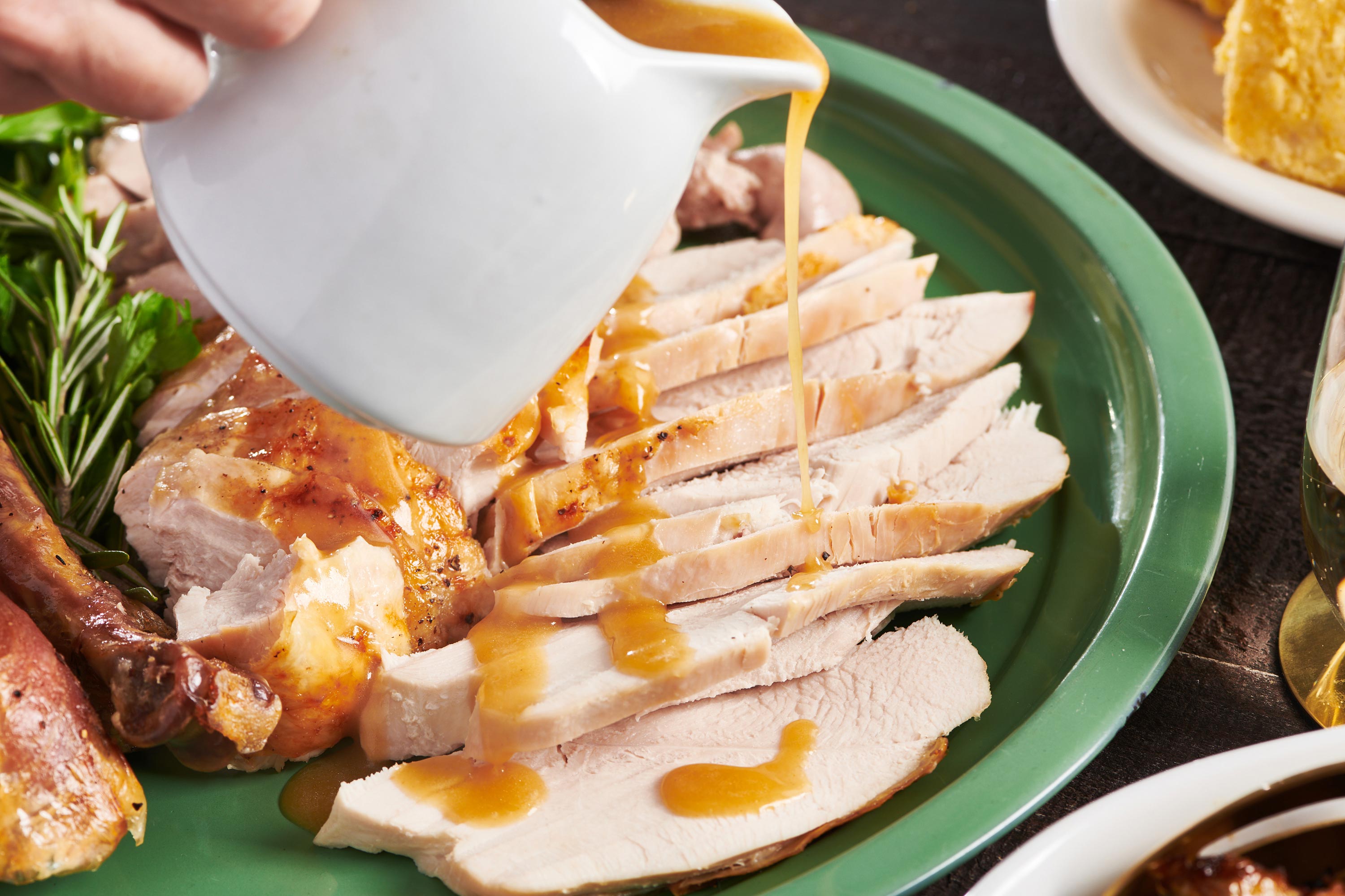 Woman pouring gravy over sliced turkey on a green platter.