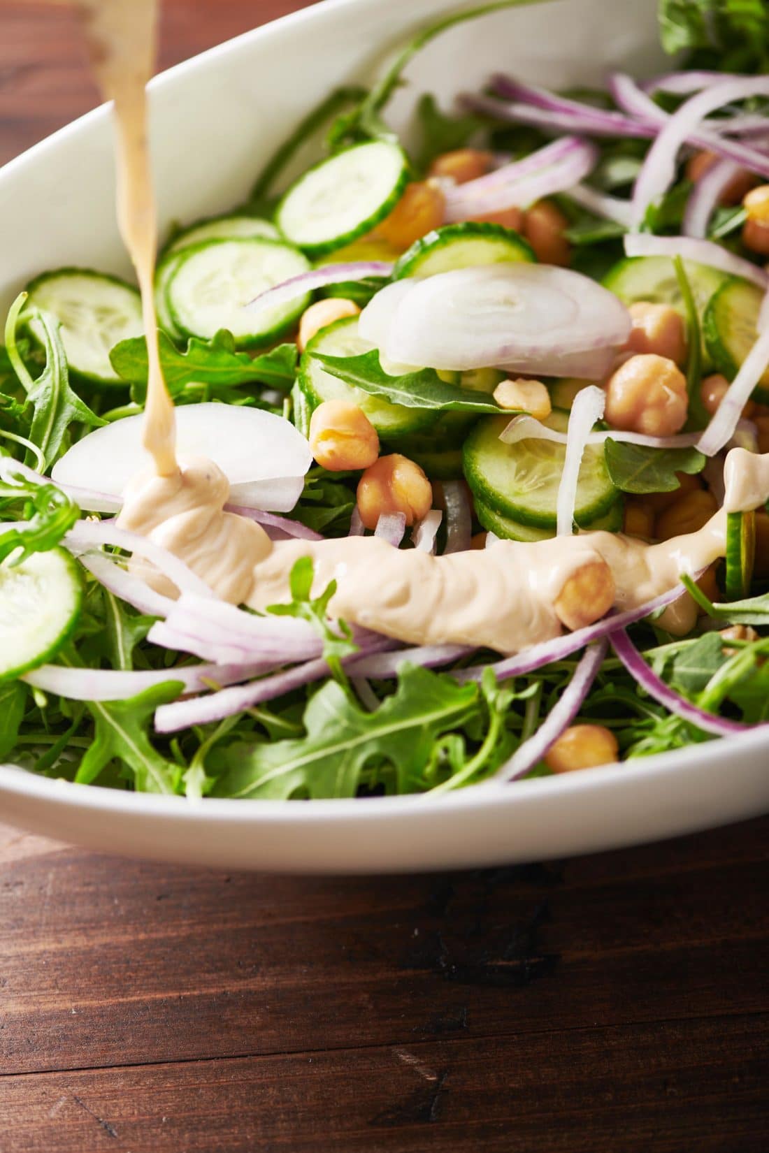 Spicy Honey Tahini Dressing pouring over a Green Salad with Chickpeas.