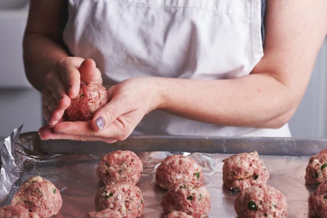 Woman forming meatballs and placing them on a foil-lined baking sheet.