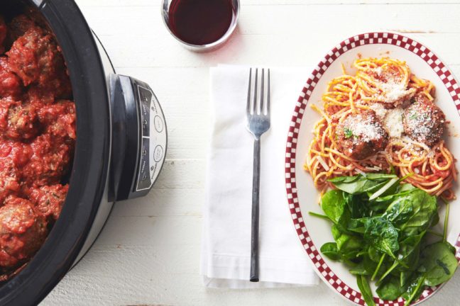 Plate of spaghetti and Italian Meatballs with spinach next to a slow cooker.