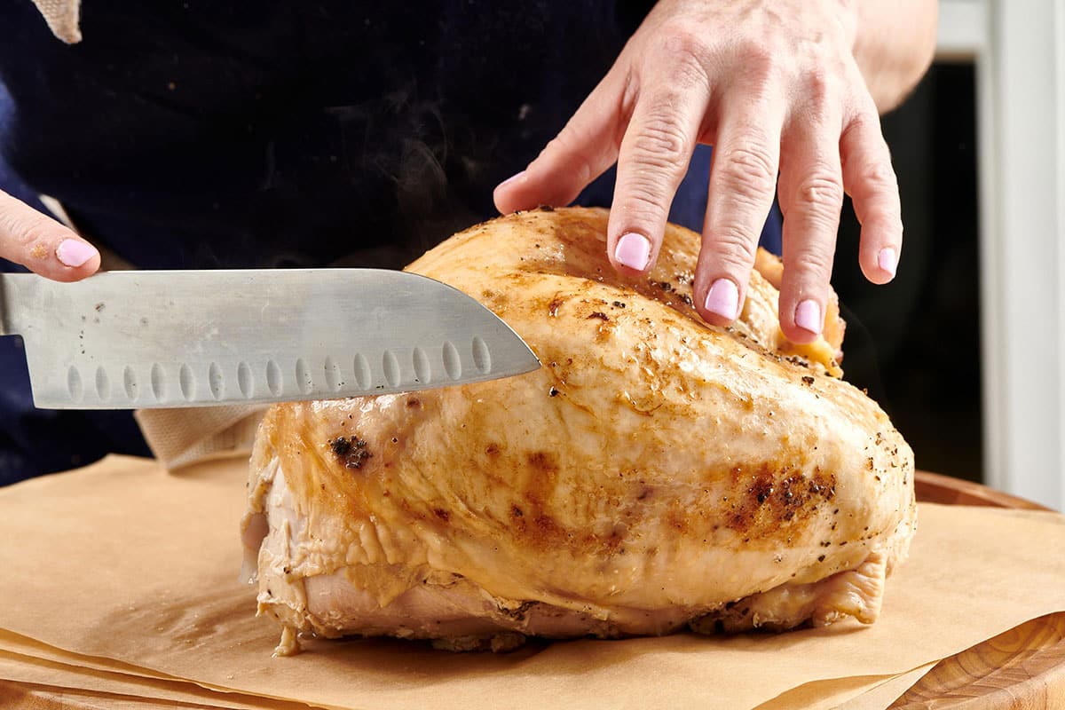 Woman cutting turkey breast with knife on cutting board.