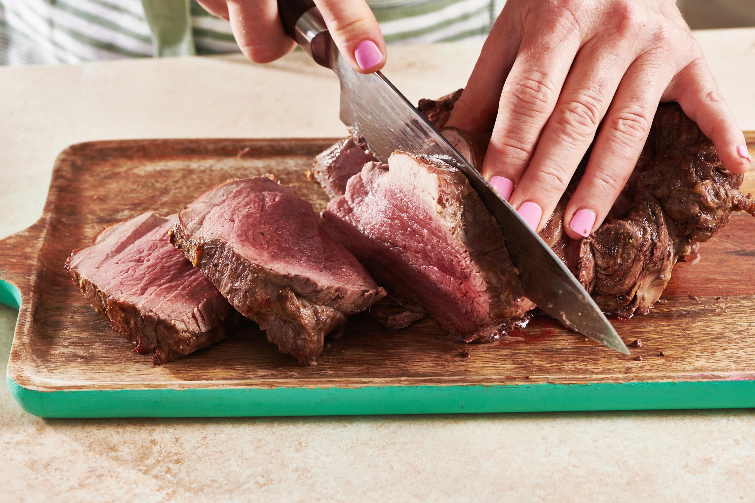 Woman slicing Beef Tenderloin Roast on wood cutting board.