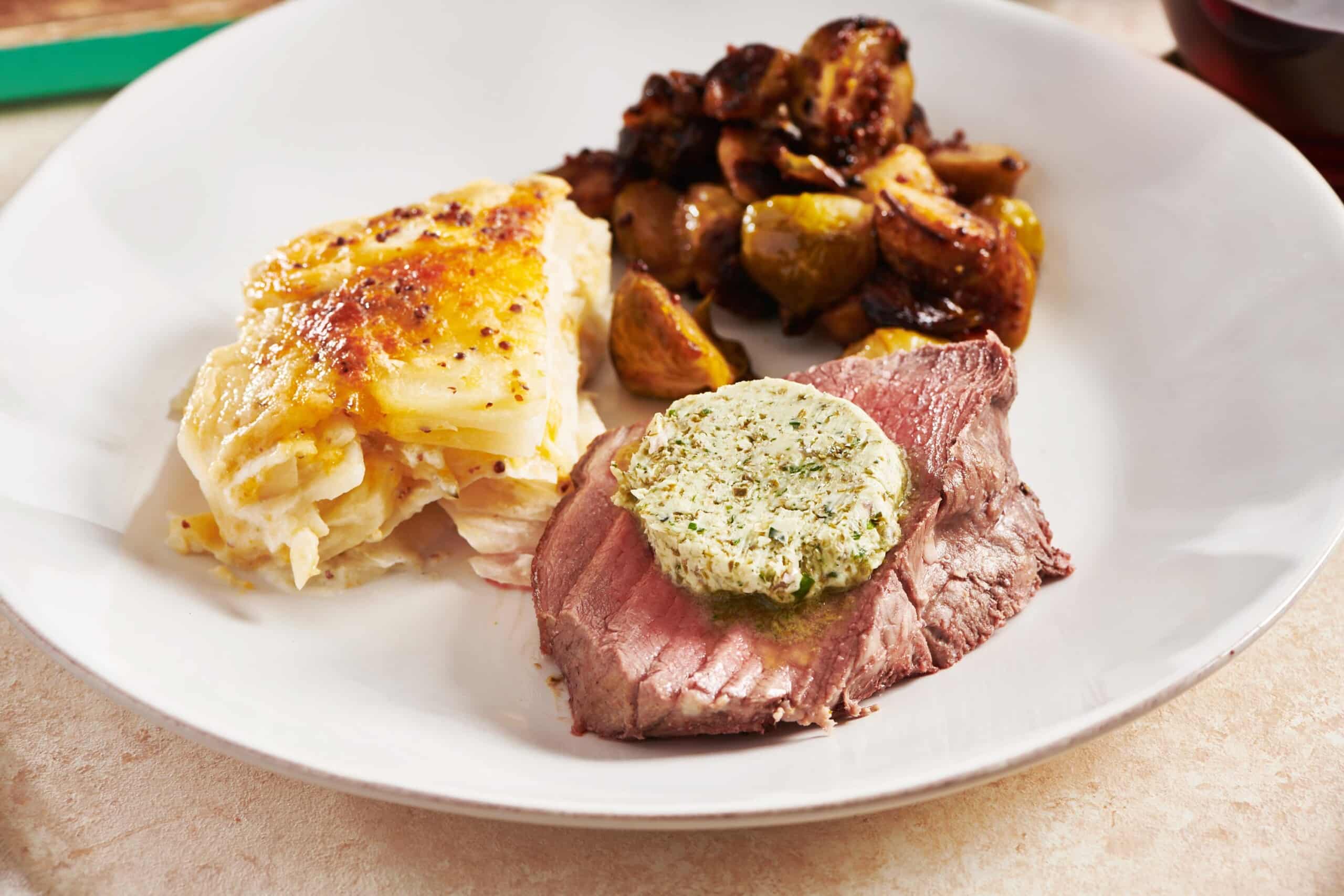 Potatoes, Brussels sprouts, and herb-butter-topped Beef Tenderloin Roast on a plate.